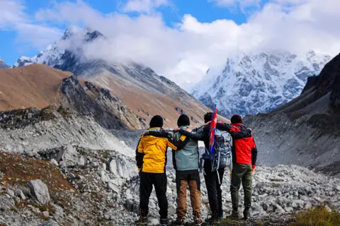 Four hikers standing arm in arm on a ridge, facing a snow-capped mountain range