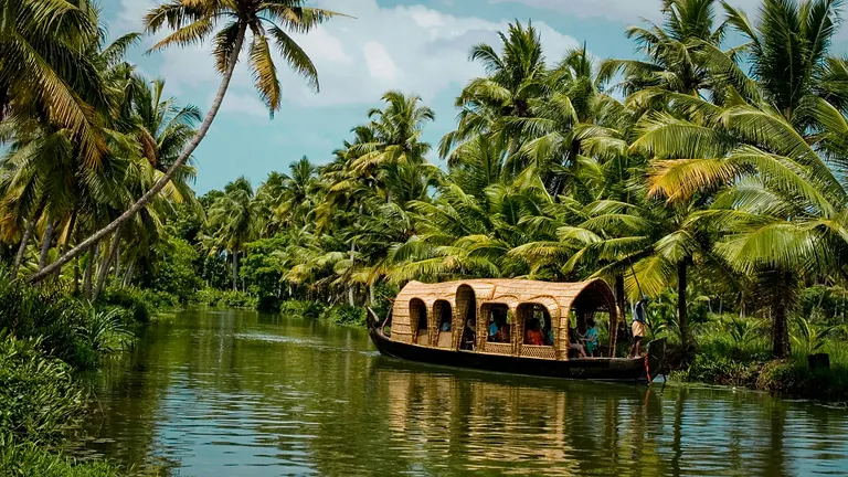A woven-canopy kettuvallam houseboat gliding down a palm-lined backwater channel
