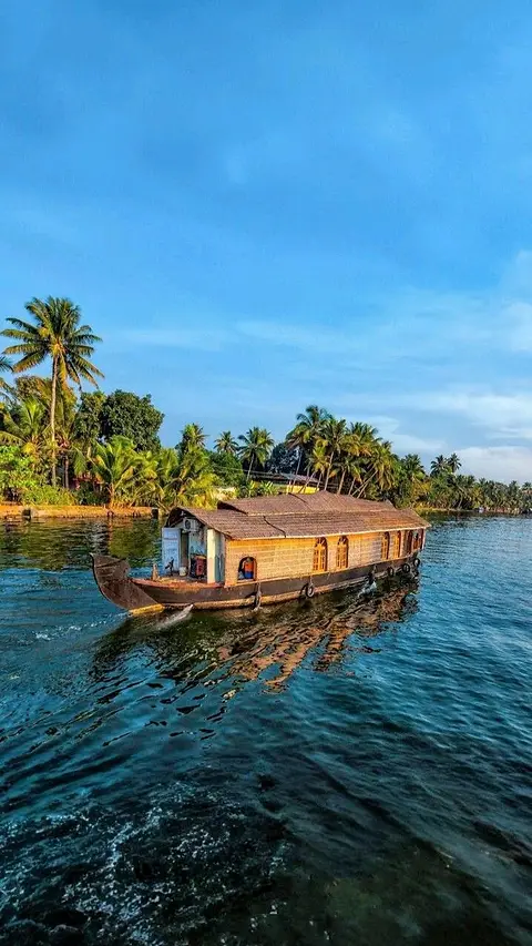 A houseboat crossing bright blue water past a palm-covered island on Ashtamudi lake