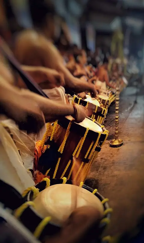Hands and sticks on a row of chenda drums mid-performance